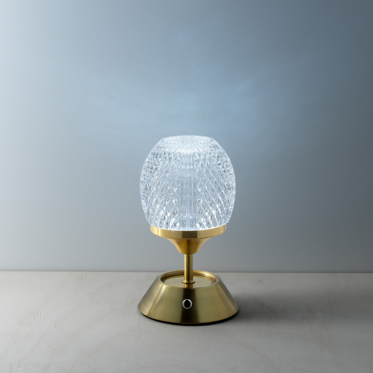 Table lamp with gold base and textured glass shade on a neutral background