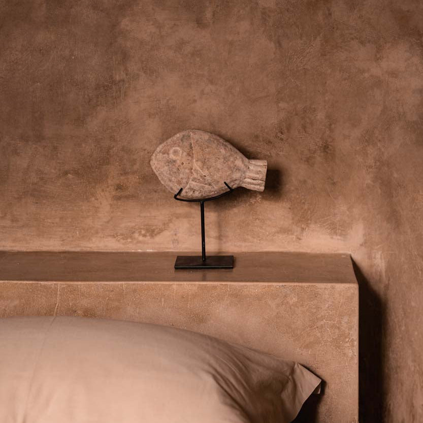 Decorative fish sculpture on a stand against a textured wall