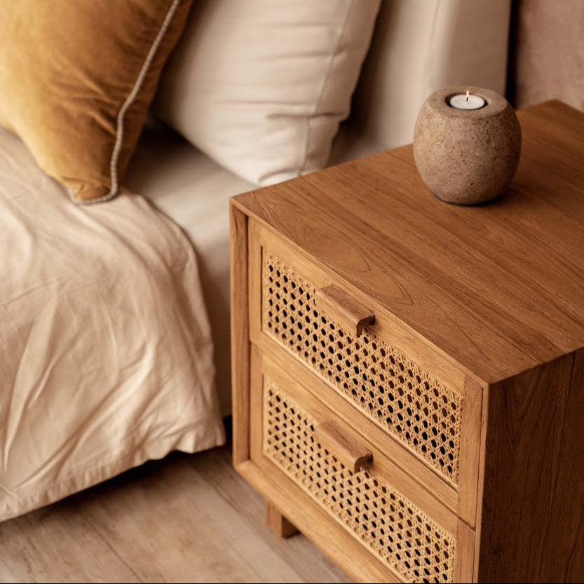 Wooden nightstand next to a bed with pillows and a candle.
