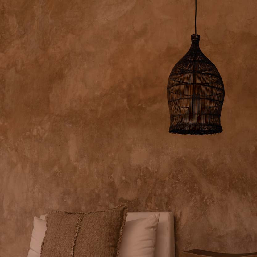 Woven bamboo pendant light hanging against a textured wall in an interior with bed.