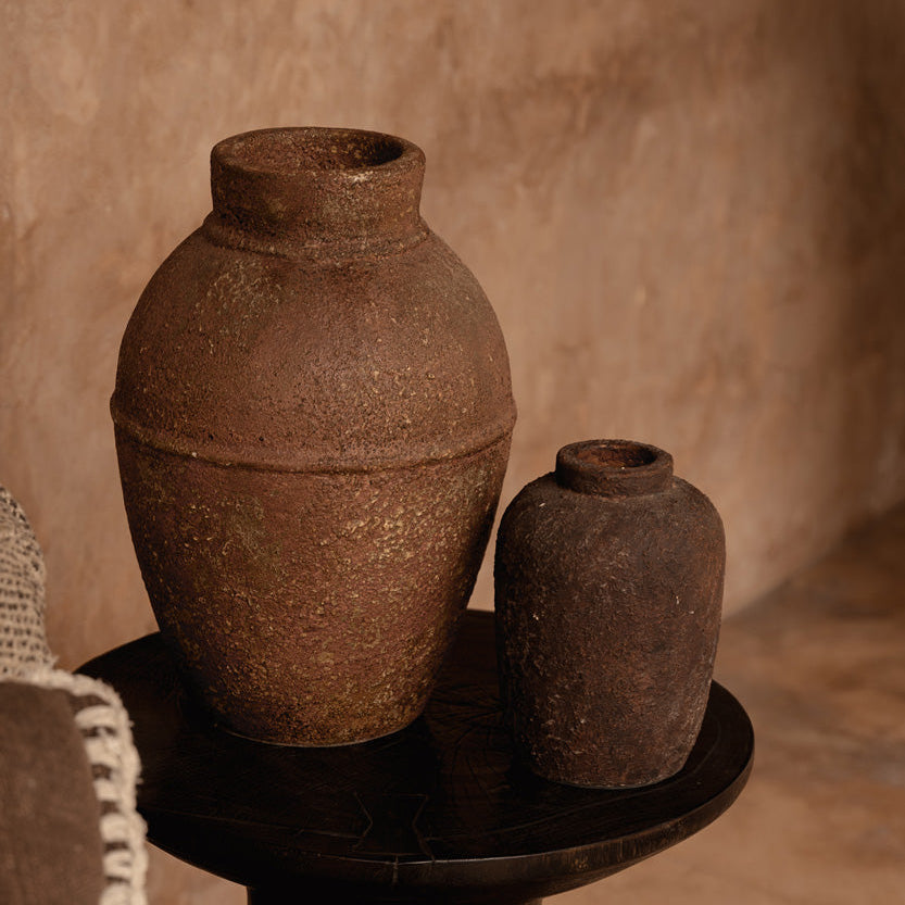 Two brown pots on a dark side table against a beige wall.