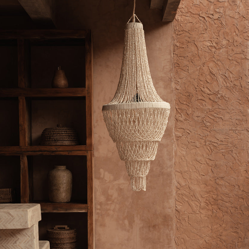 Beige chandelier hanging from a ceiling in a room with shelves and decorative items.