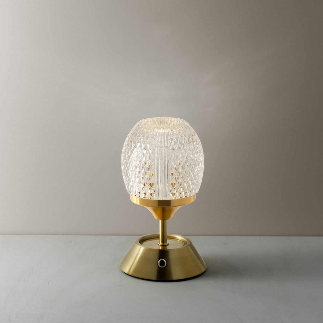 Table lamp with gold base and textured glass shade on a warm background