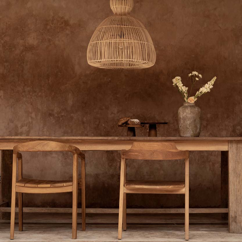 Wooden dining table with chairs against a textured brown wall with pendant light.