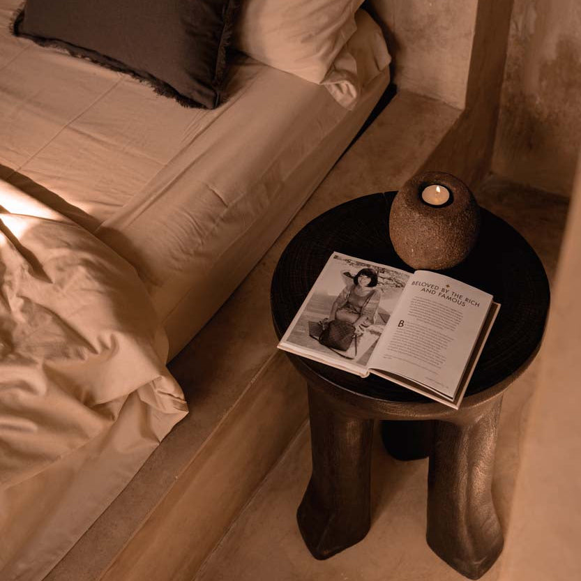 Bedroom scene with a bed and a side table featuring an open magazine and candle holder