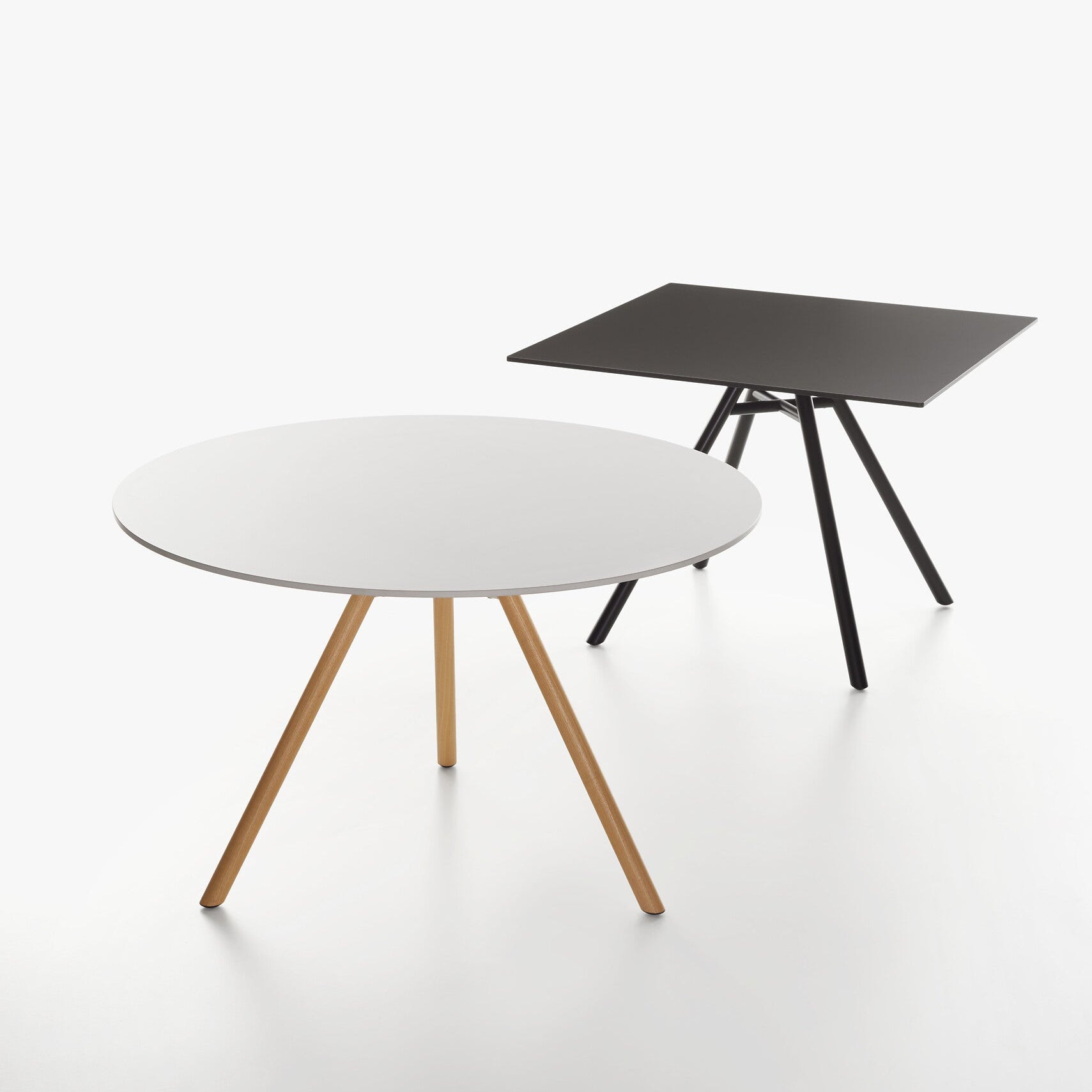 Two modern MART tables on a seamless white studio background. The front table is round with a white top and the second is square table with black table top. 