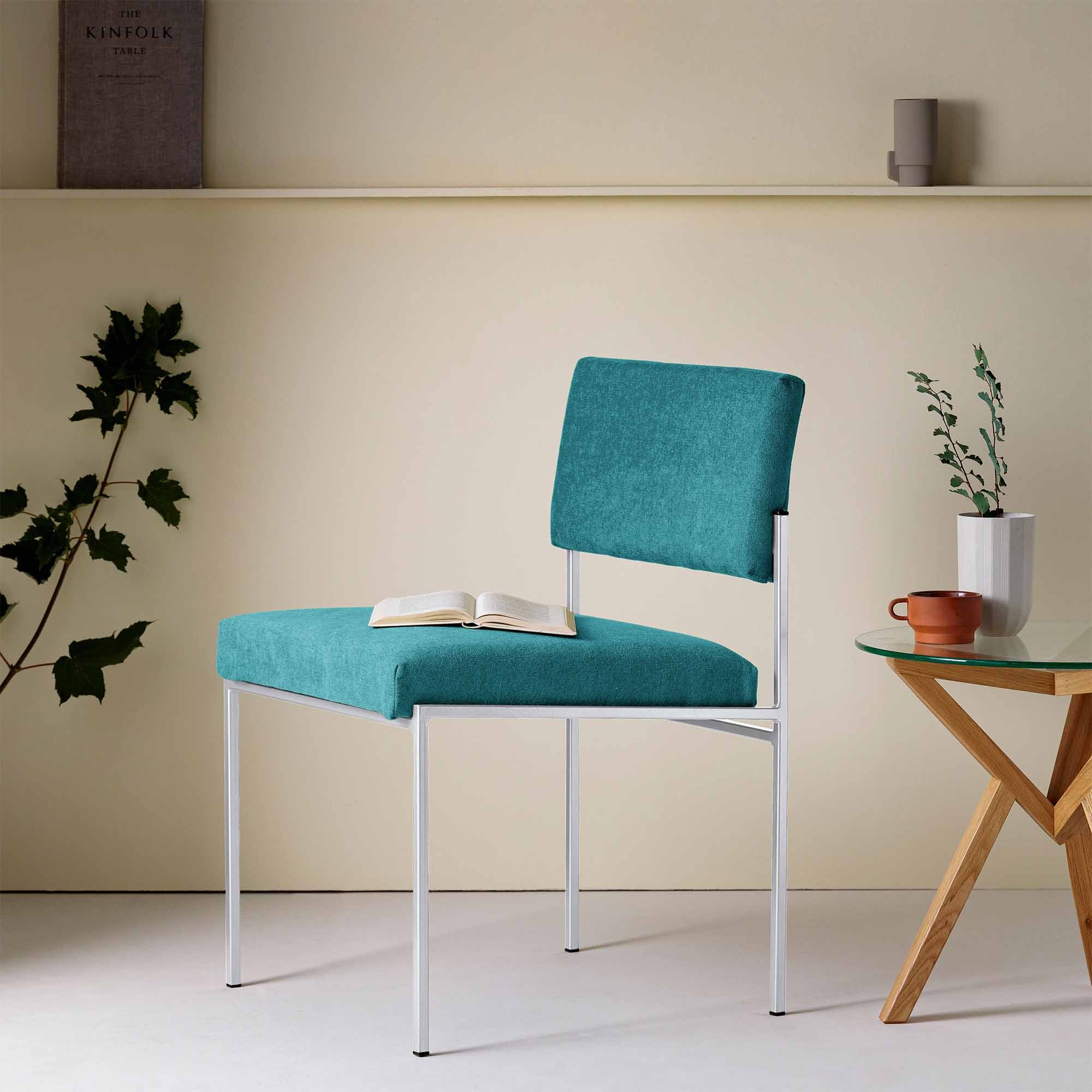  Chair, Powder-Coated Steel Frame blue fabric, white frame, interior half-side view with table and book